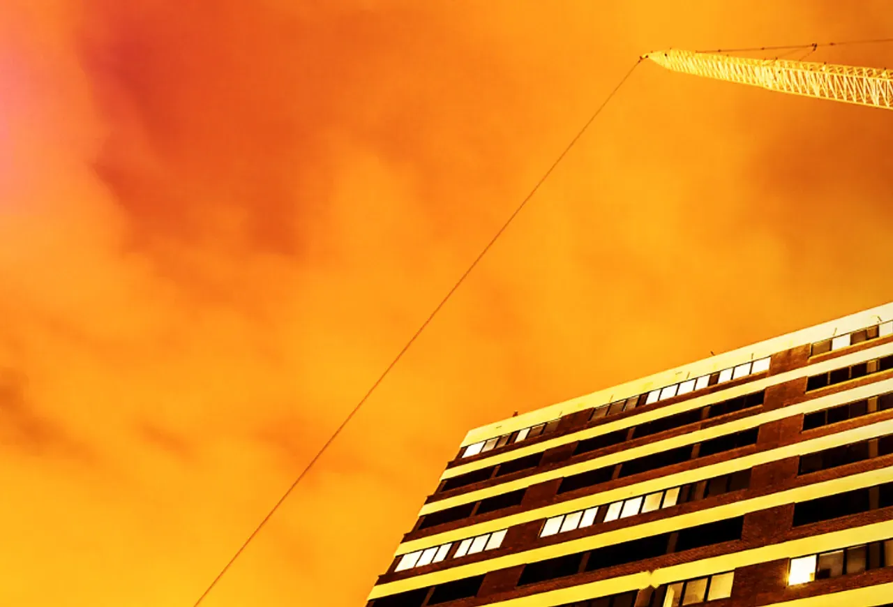 Luffing tower crane jib above a city building at sunset