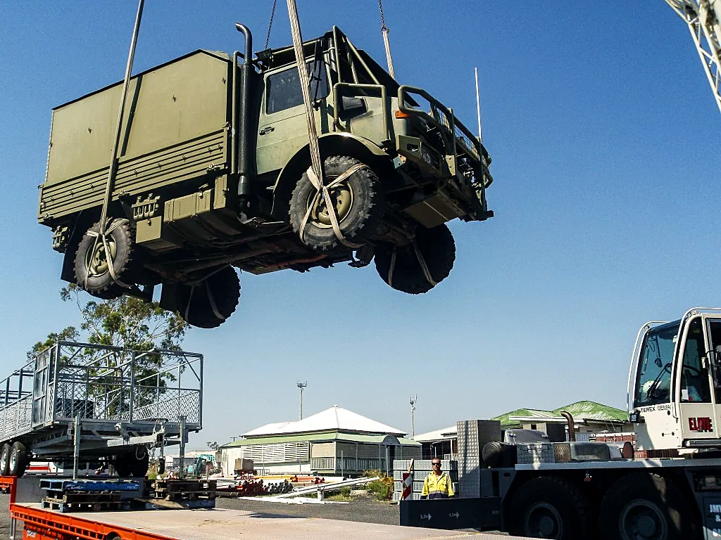 Crane lifting an off-road truck in soft slings above a trailer